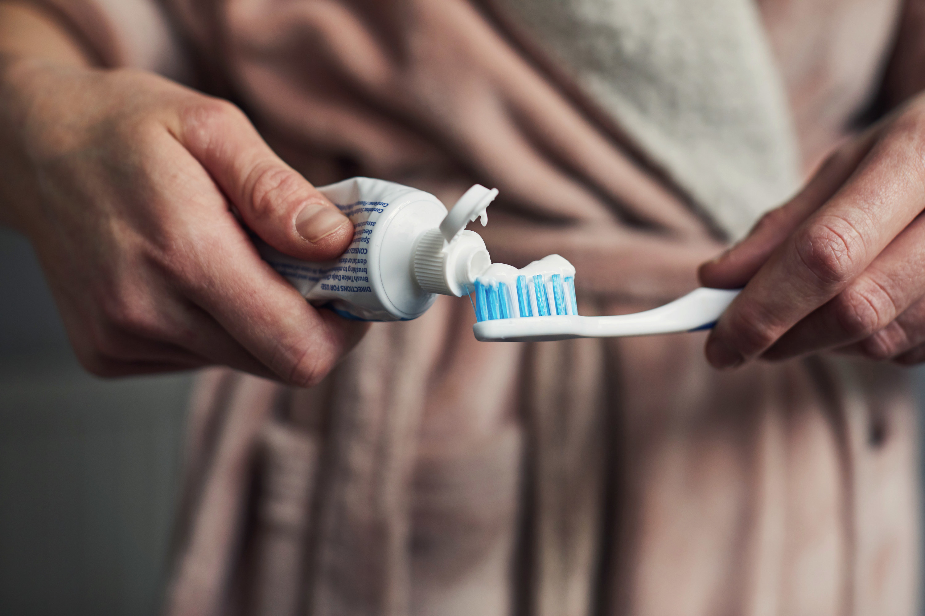 close up of a person putting toothpaste on a toothbrush