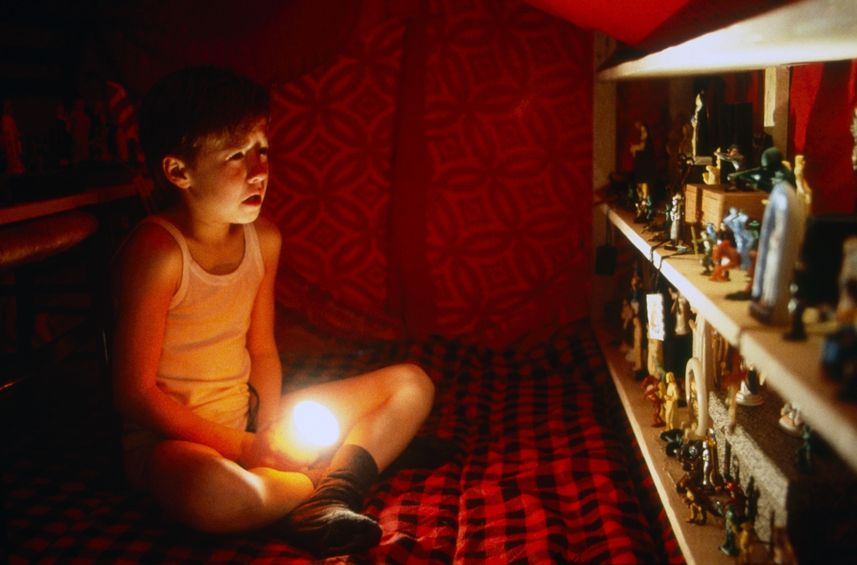 young kidding sitting inside a fort with a flashlight looking at his toys