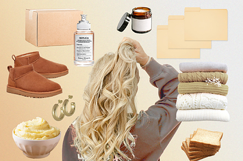 The back of a woman's head and clean, cozy, pale objects including folded sweaters, bread, earrings, perfume, and candles