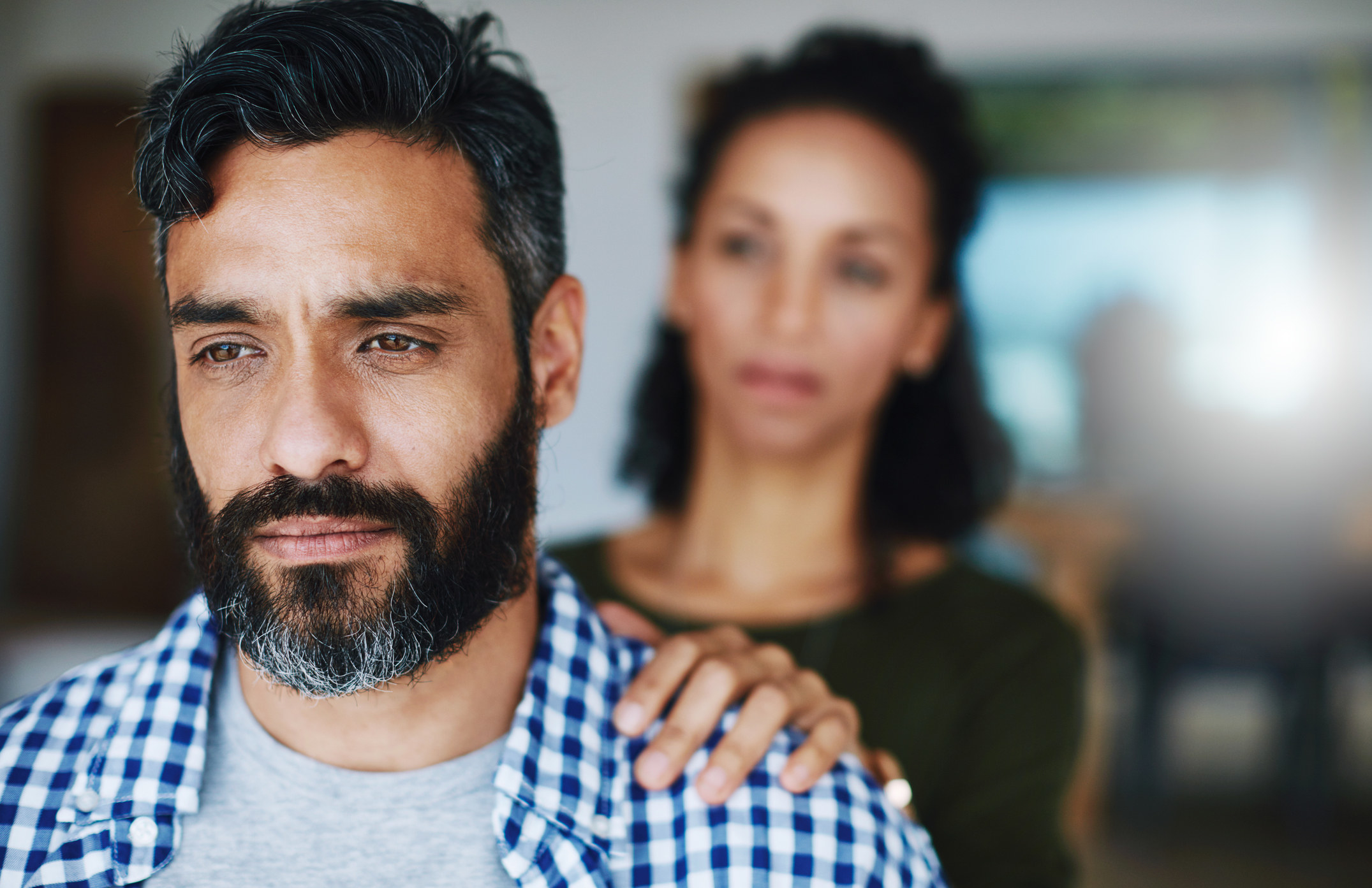 A man looking sad as his wife places her hand on his shoulder