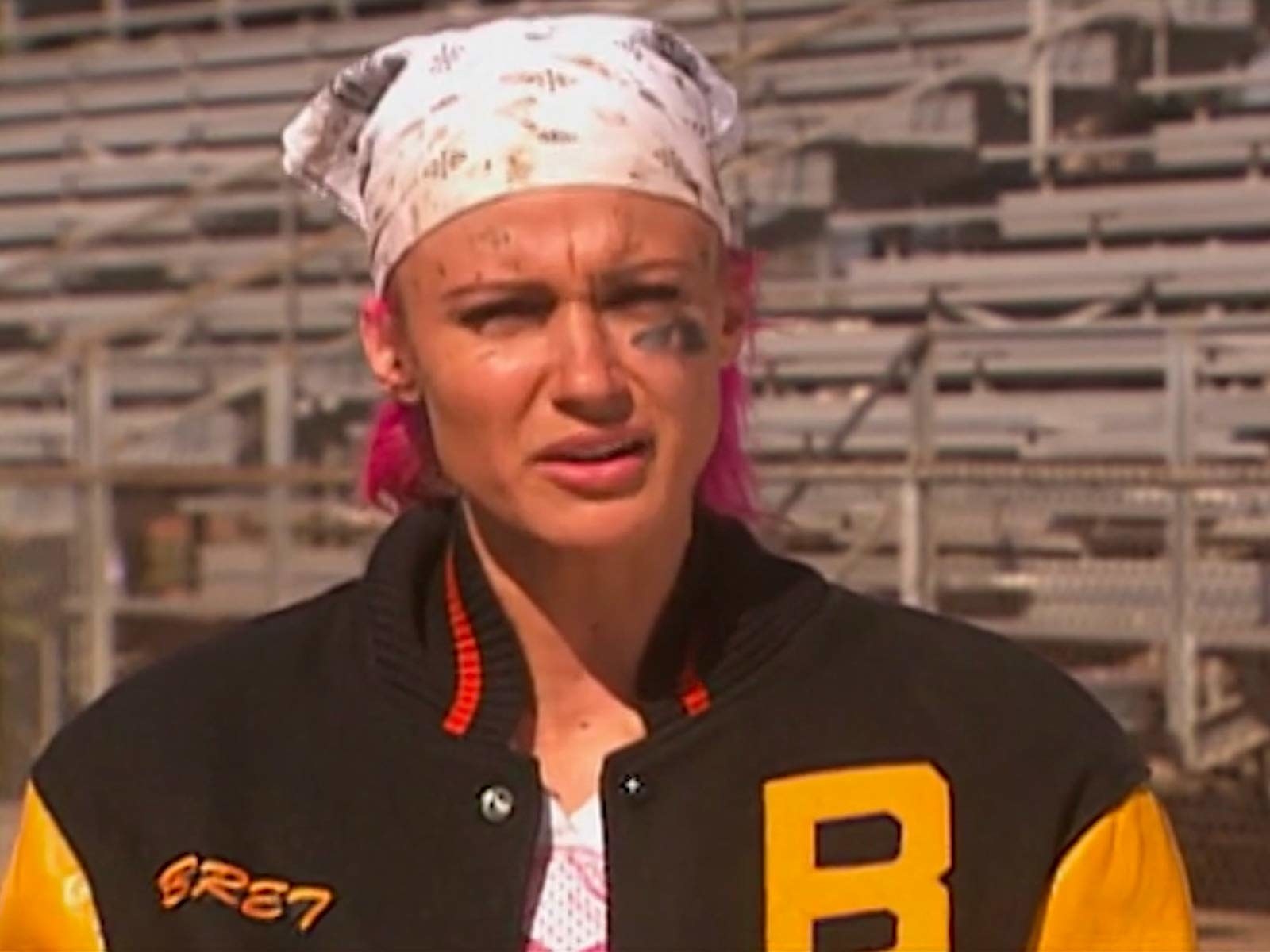 girl with short hair wears a bandana and a letterman jacket, mud smeared on her face