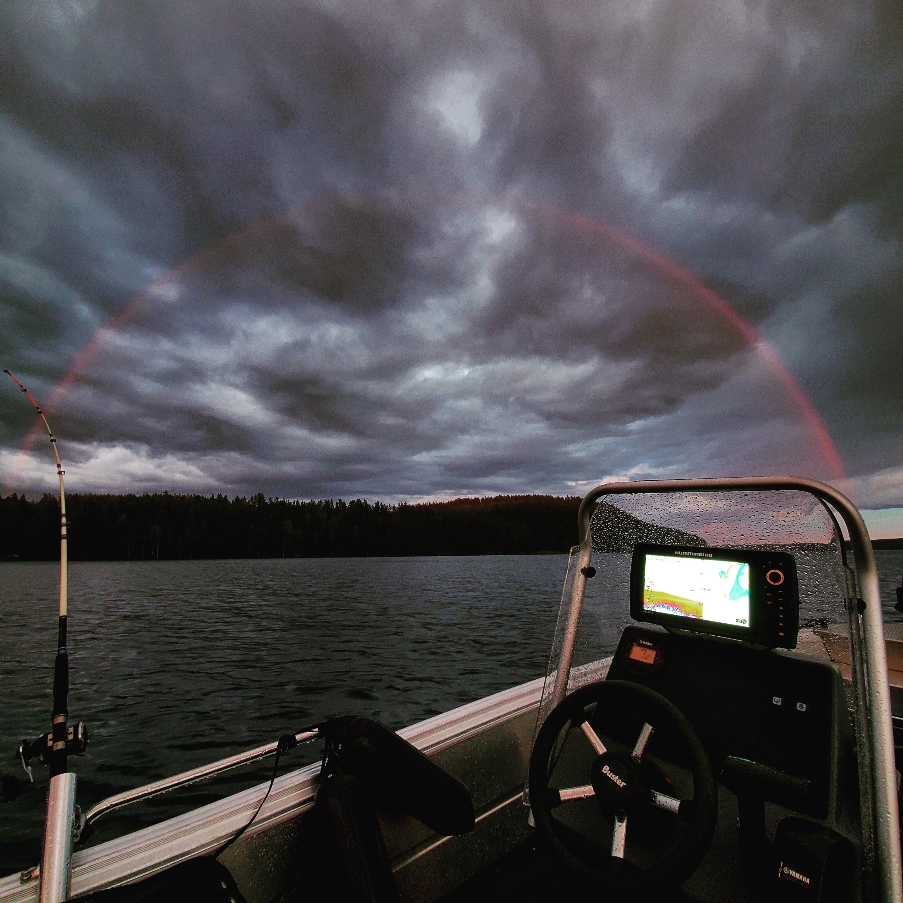 a boat out on a lake, a cloudy night, and a full arc rainbow that&#x27;s only red