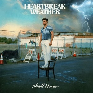 cover for &quot;Heartbreak Weather&quot; which is him standing on a chair, wearing chinos and a button down short sleeved shirt