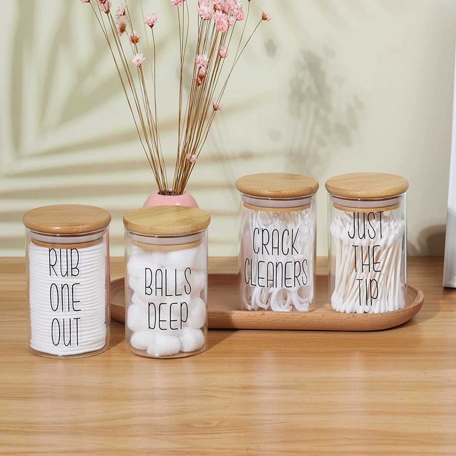 a set of glass apothecary jars with saucy labels filled with bathroom essentials
