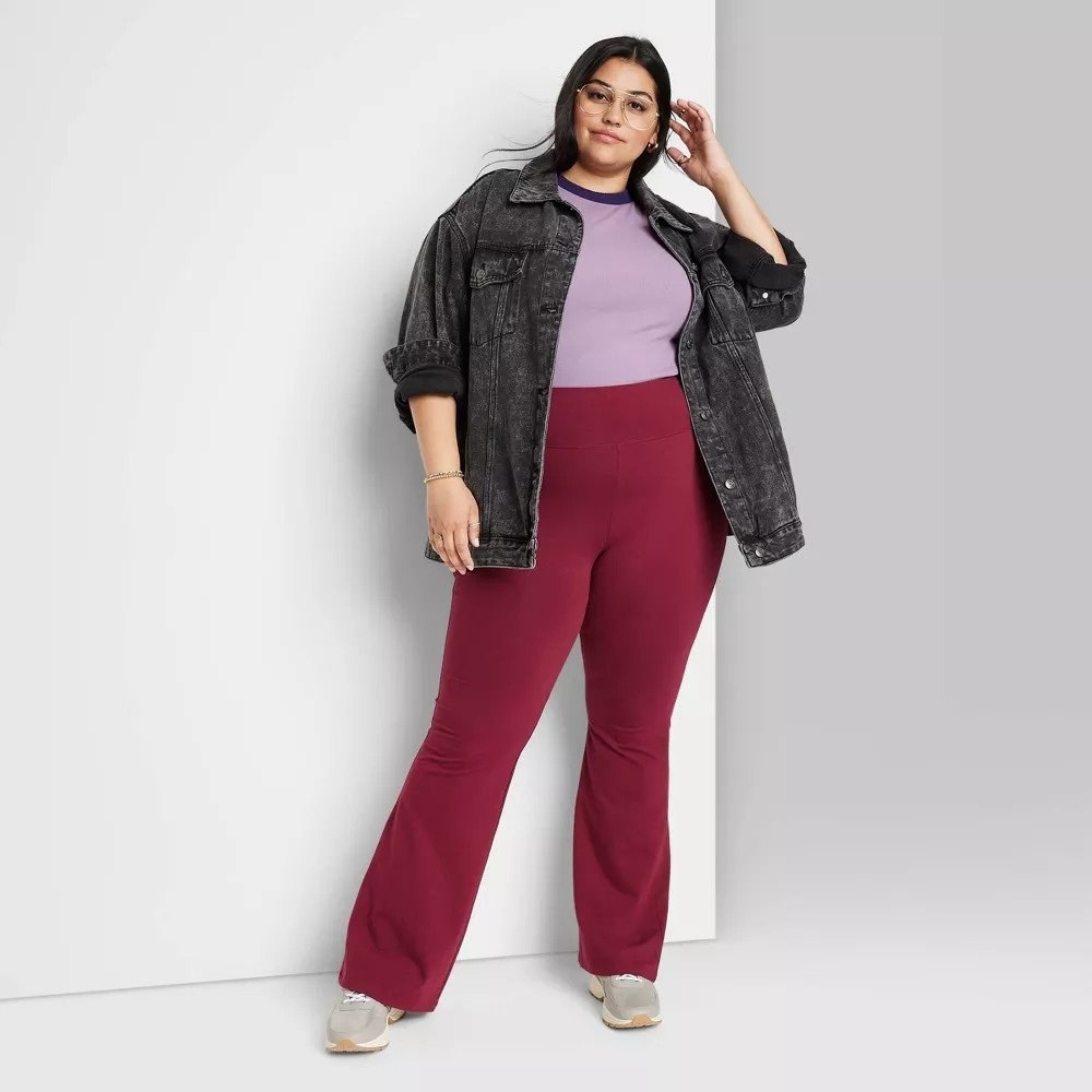 Model wearing red flare leggings with purple shirt and black denim jacket