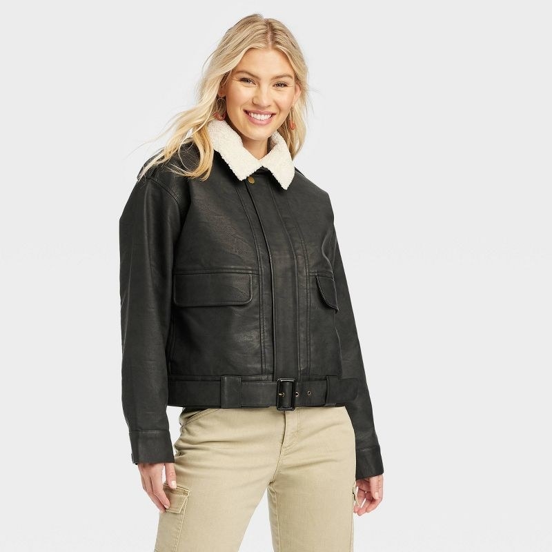 Model wearing black faux leather bomber with white sherpa collar