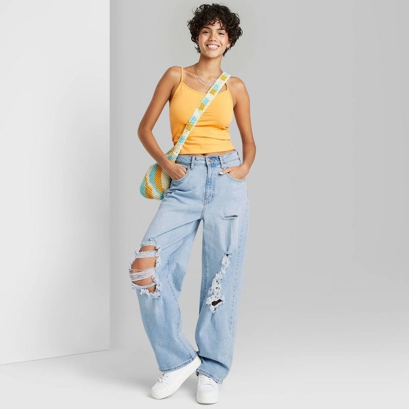 Model wearing light wash, baggy, torn jeans with orange cami