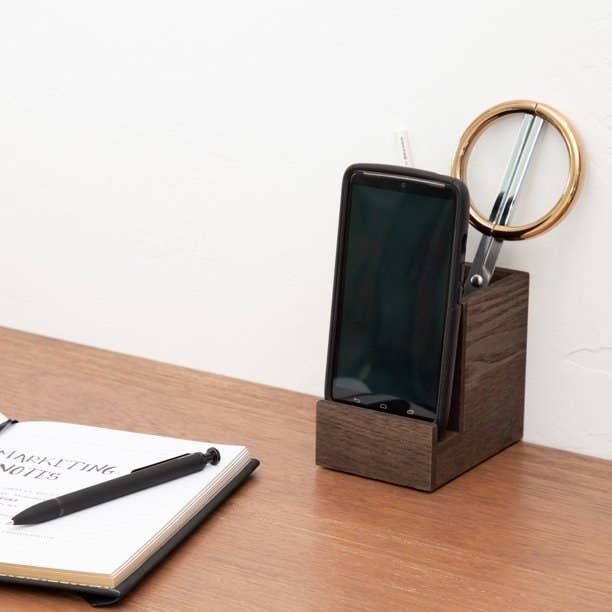 a wooden pen holder holding a phone and office supplies