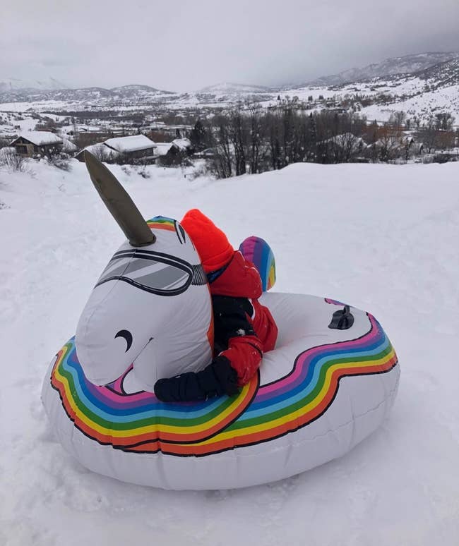 reviewer's photo of their child sitting on the unicorn snow tube