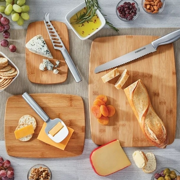 a three-piece wood cutting board holding cheeses and rustic a baguette