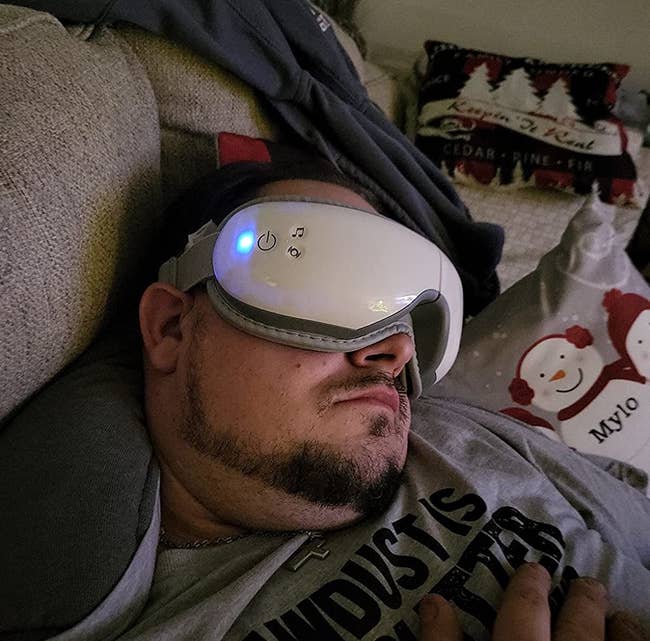 Reviewer falling asleep on couch with heated eye massager on face