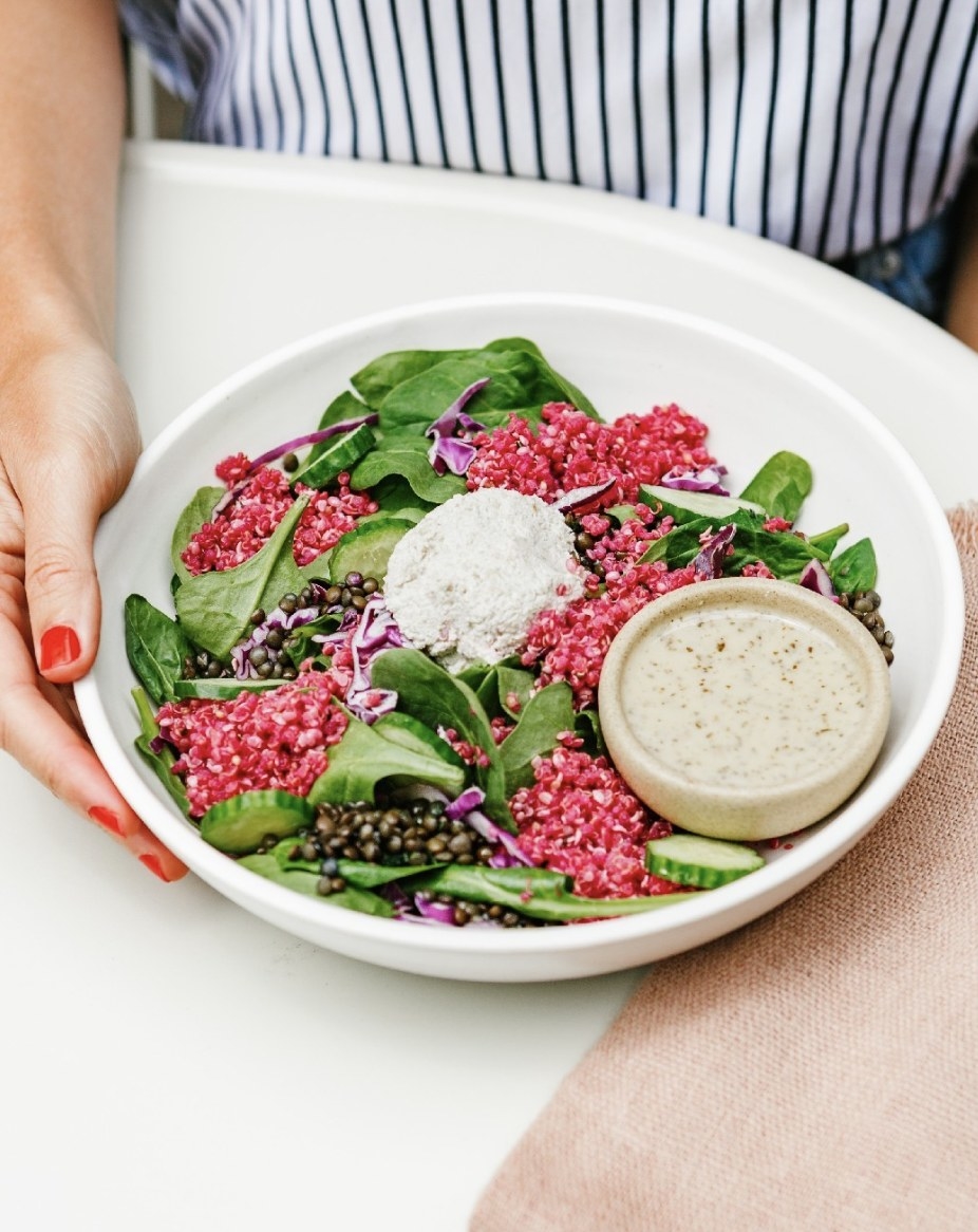 A salad featuring greens, shredded beets, lentils, cucumbers, and dressing with dollop of creamy sauce