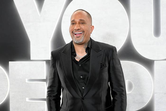 A close-up of Kenya Barris smiling widely at an event for &#x27;You People&#x27;. He is wearing a suit and a chain