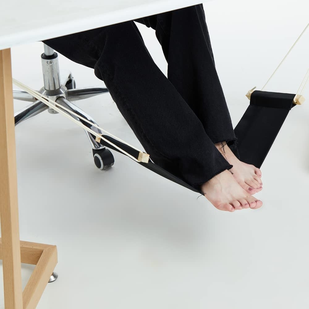 someone&#x27;s feet inside the foot hammock under a desk