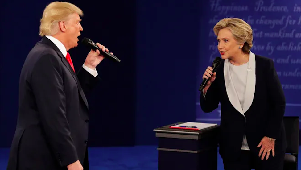 Donald and Hillary closer together, holding microphones onstage, and looking at each other