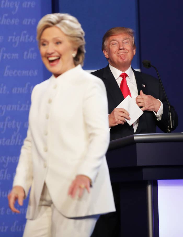 Hillary smiling and standing in front of Donald onstage