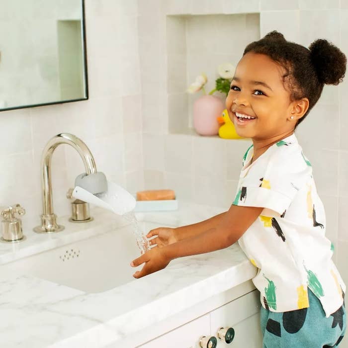 Child model washing hands at sink with aid of faucet extender