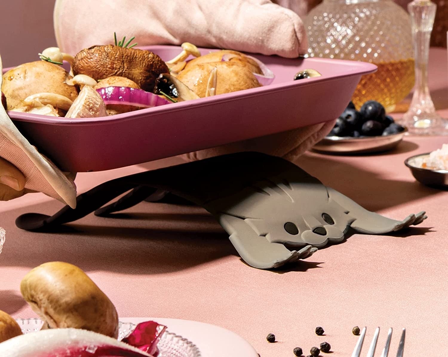someone setting a hot dish on the cat-shaped silicone trivet
