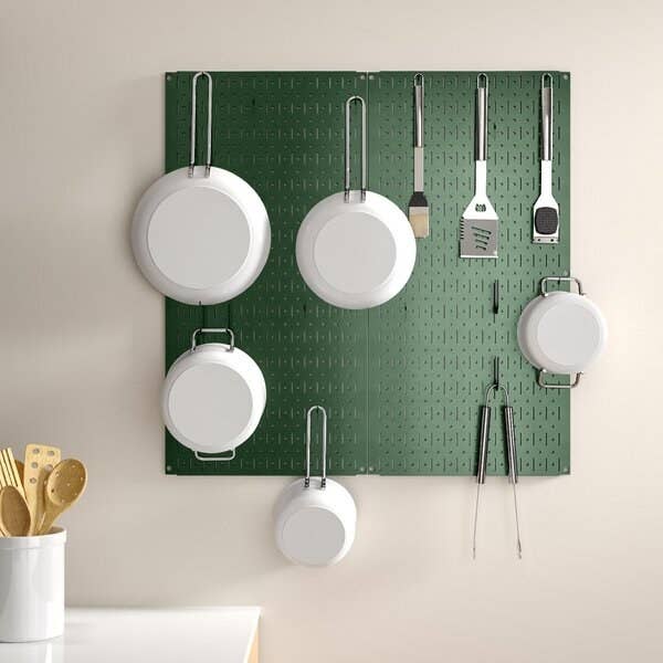 Pans, spatulas, and other kitchen tools hanging from the pegboard in green