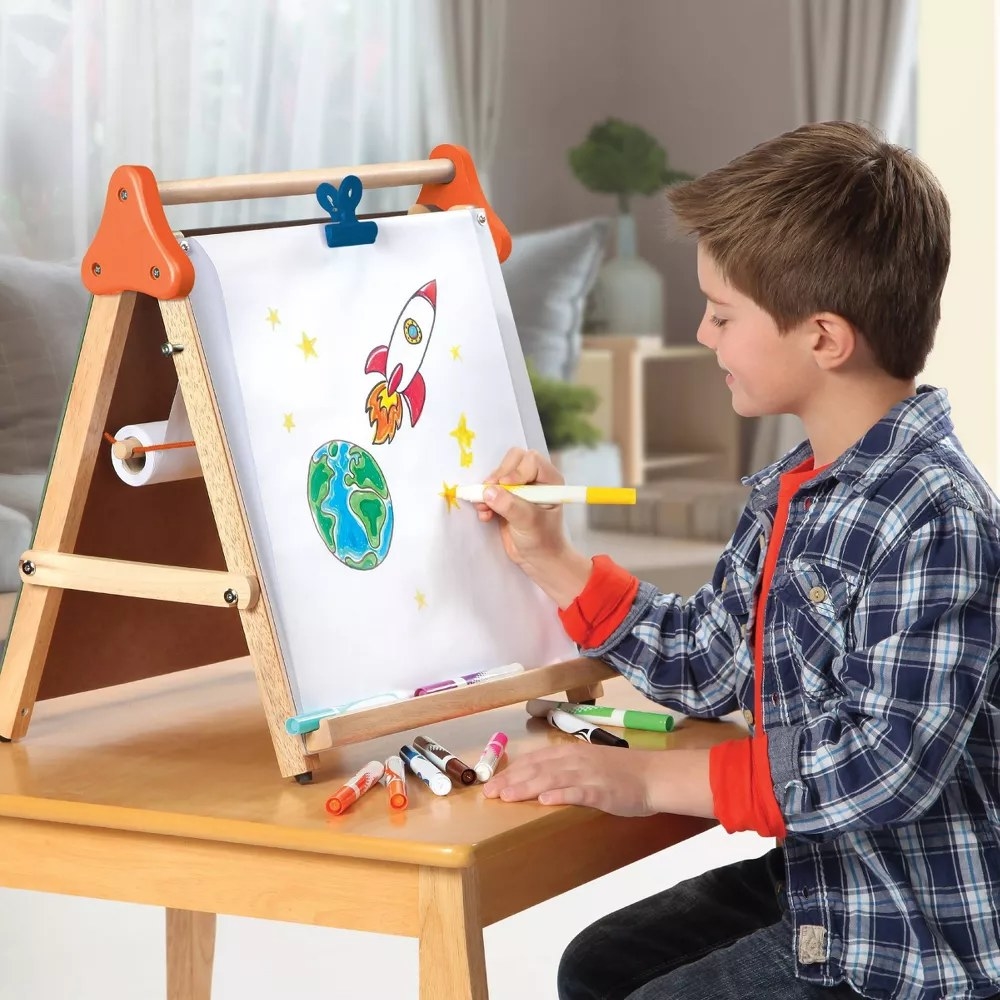 Child model drawing with markers on wooden easel