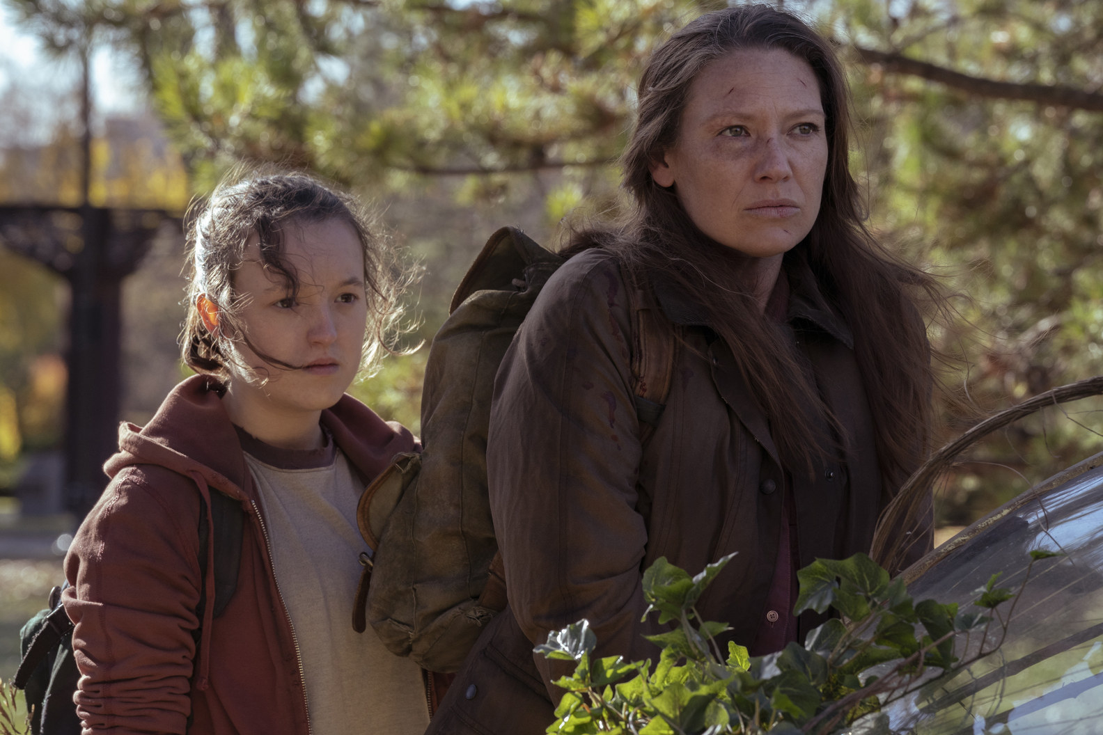 Bella Ramsey and Anna Torv look disheveled as they wanted through trees in the show