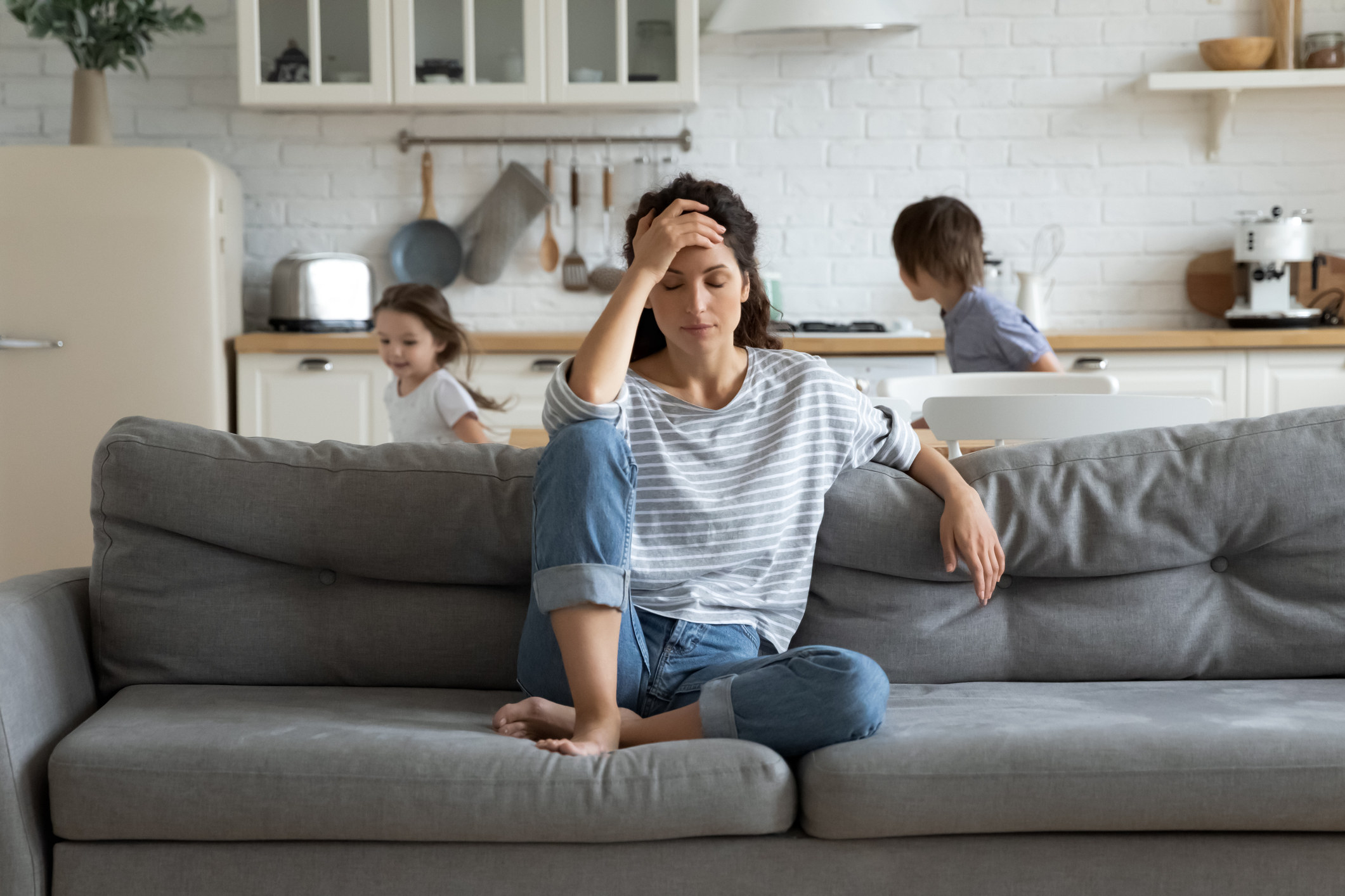 mom stressed on the couch while child play behind her
