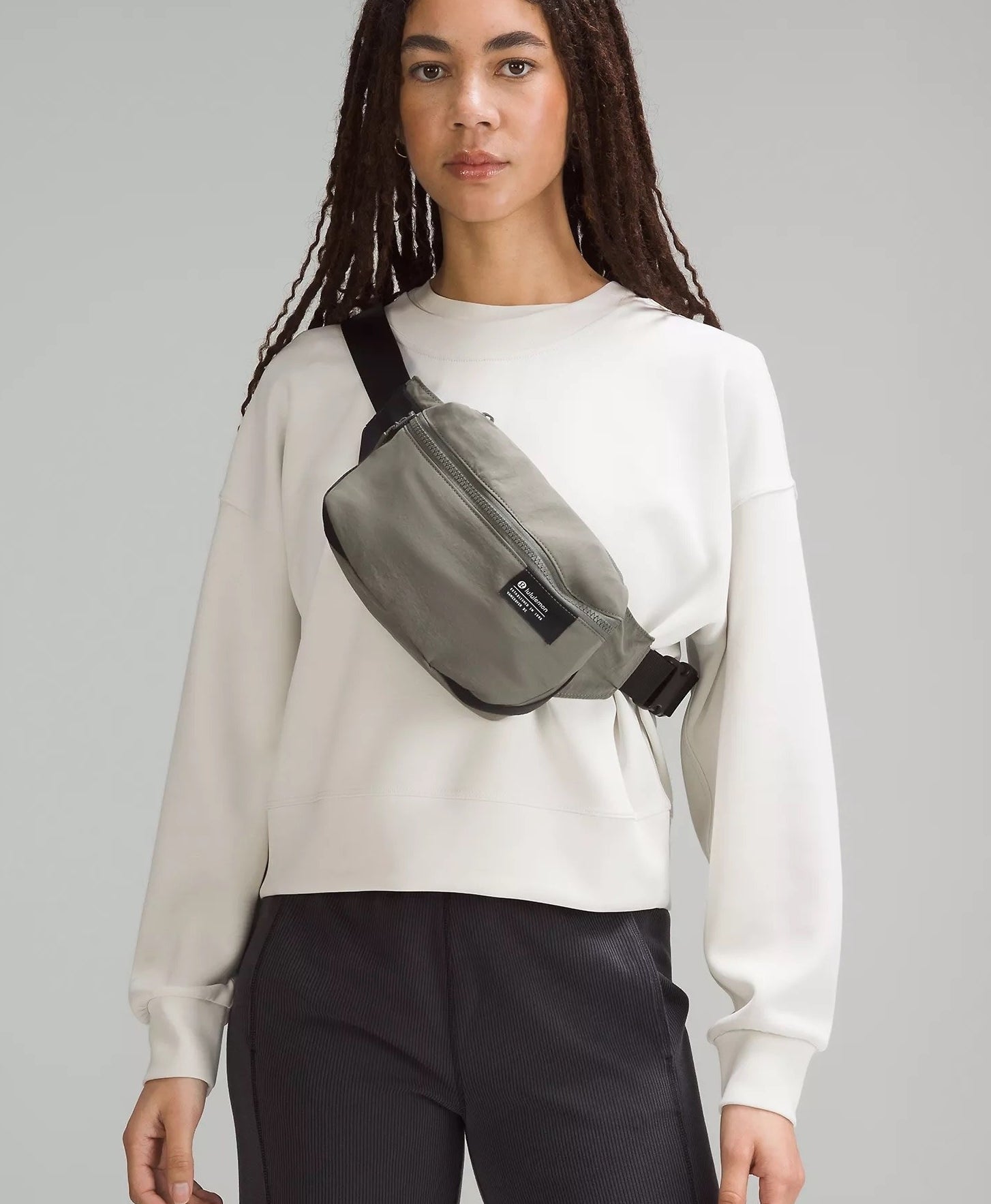 a model wearing the belt bag over a sweater in front of a plain background