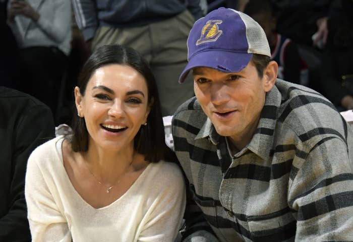 Mila and Ashton smiling as they sit at a casual event