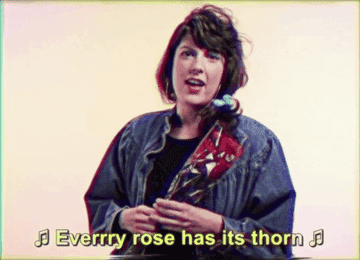 woman in a denim jacket holding a bouquet of roses in plastic wrap singing every rose has its thorn