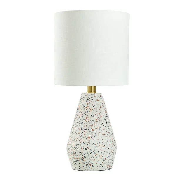 A speckled table lamp with white lamp shade