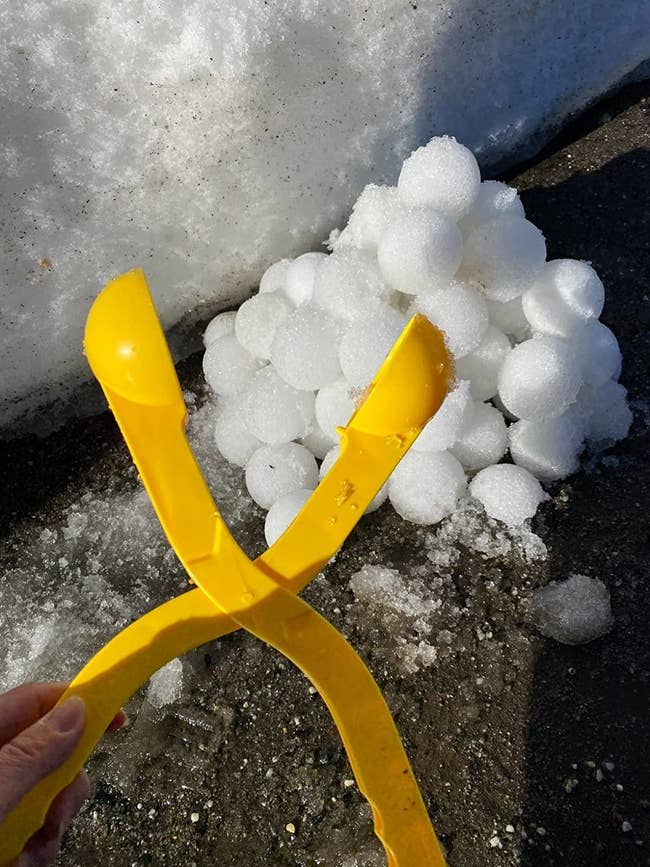 reviewer's photo of the yellow snowball maker tool near a pile of snowballs