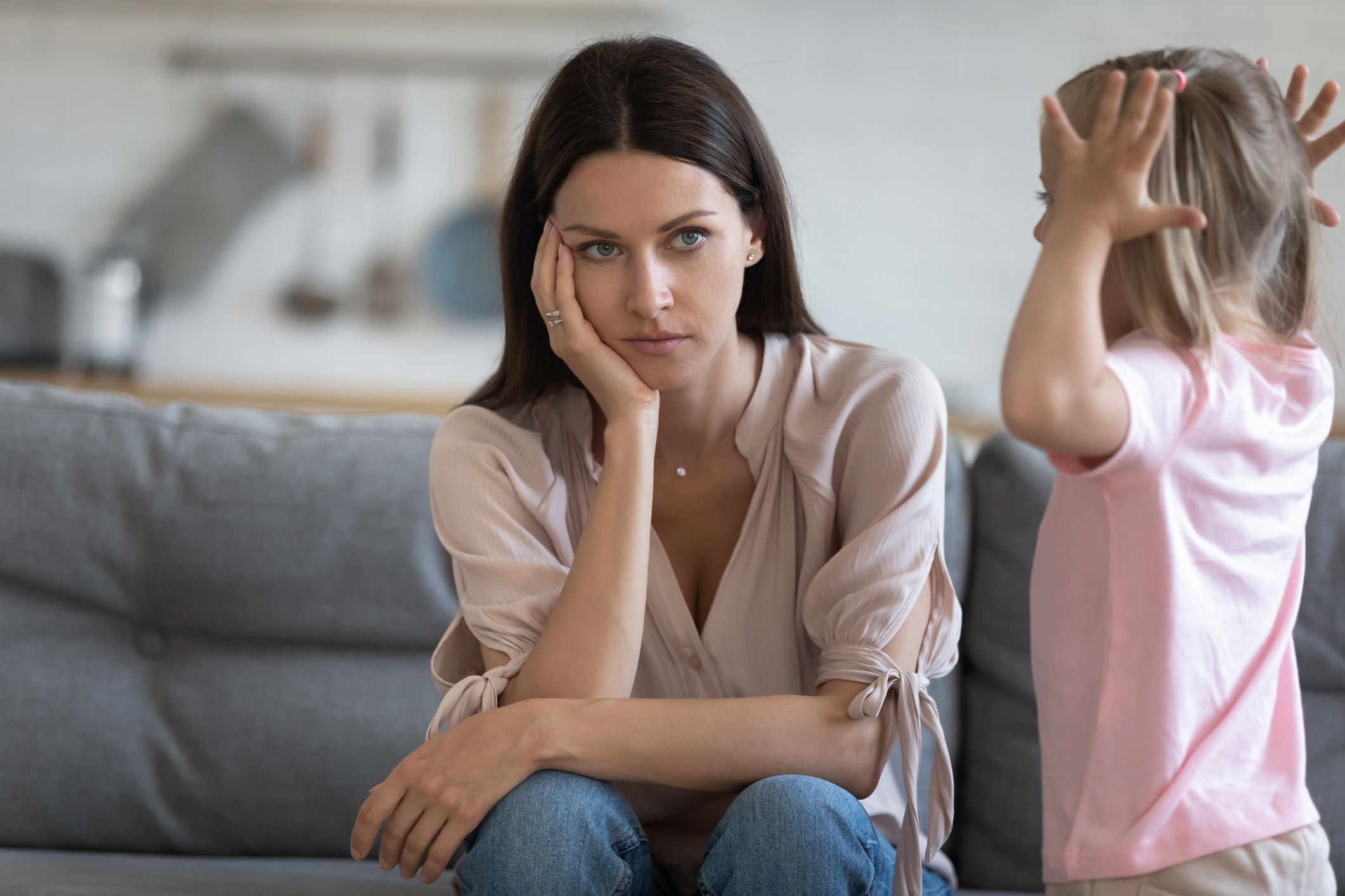 Glum-looking woman sitting on a couch with a child standing next to her