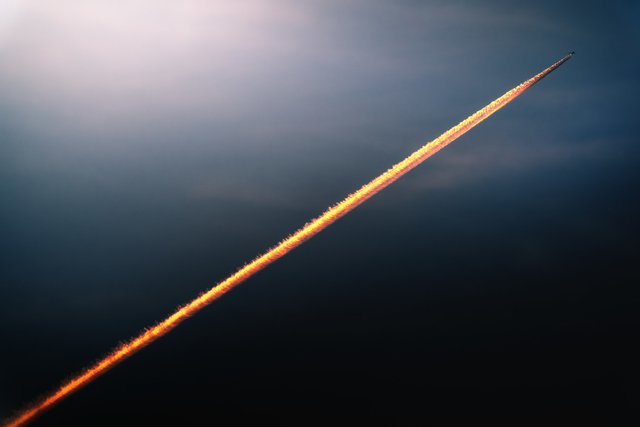 An airplane in high flight and the wake it leaves behind, colored by the sunset light and looking like a rocket