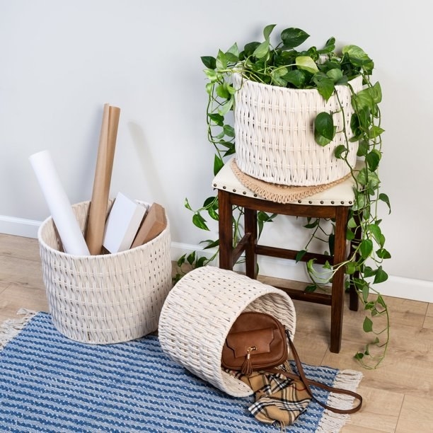a three-piece wicker basket set holding a plant, purse, blanket, and paper