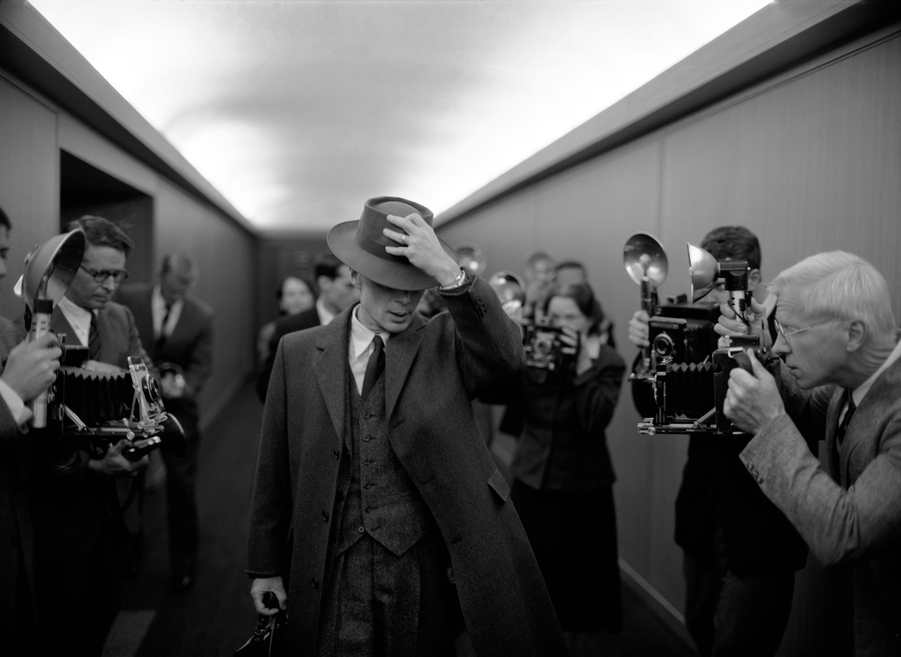 A man in a hat and suit walks through a hallway full of photographers