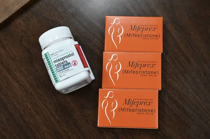 A medication canister and some cardboard boxes labeled misporostol and mifepristone lie on a table