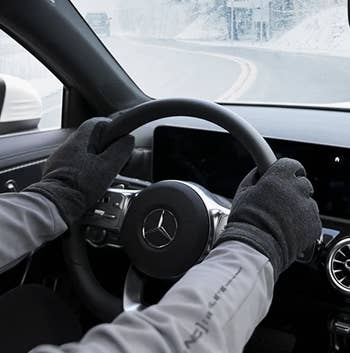 Model wearing the gloves in grey-black while gripping a steering wheel