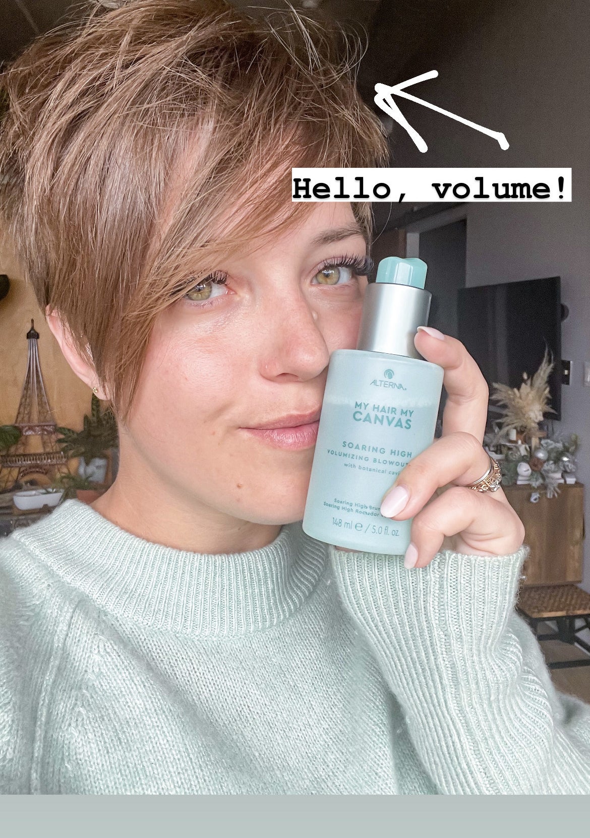 victoria holding up a bottle of the blowout spray; her hair has volume and texture