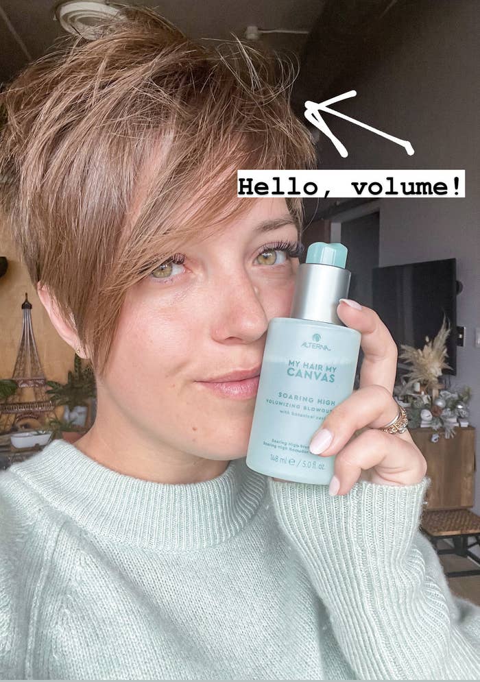 victoria holding up a bottle of the blowout spray; her hair has volume and texture