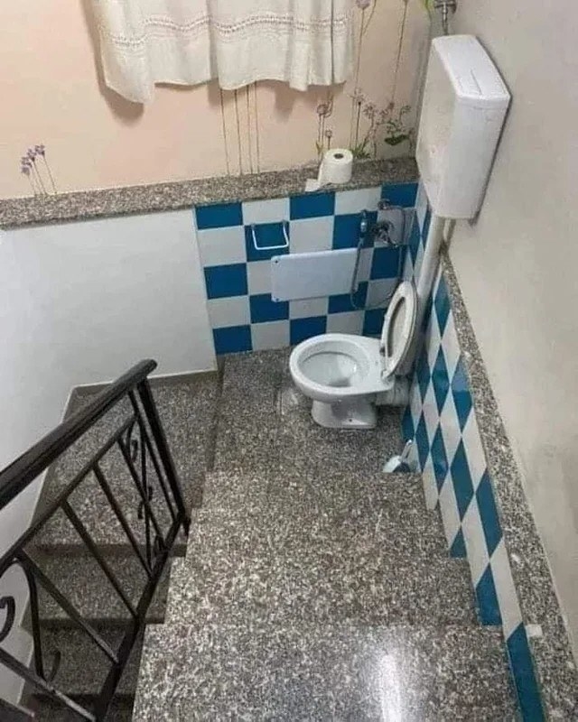 a toilet on the landing of a flight of stairs with absolutely no privacy