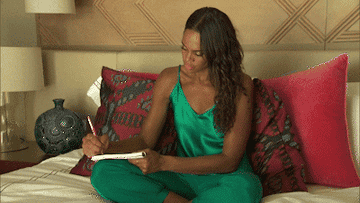 A woman sitting in bed with her legs folded and writing in a journal