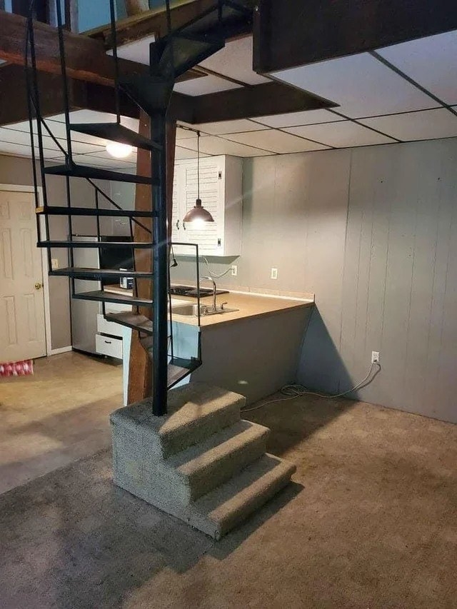 a spiral staircase ascending from three carpeted stairs and joined to a kitchen countertop