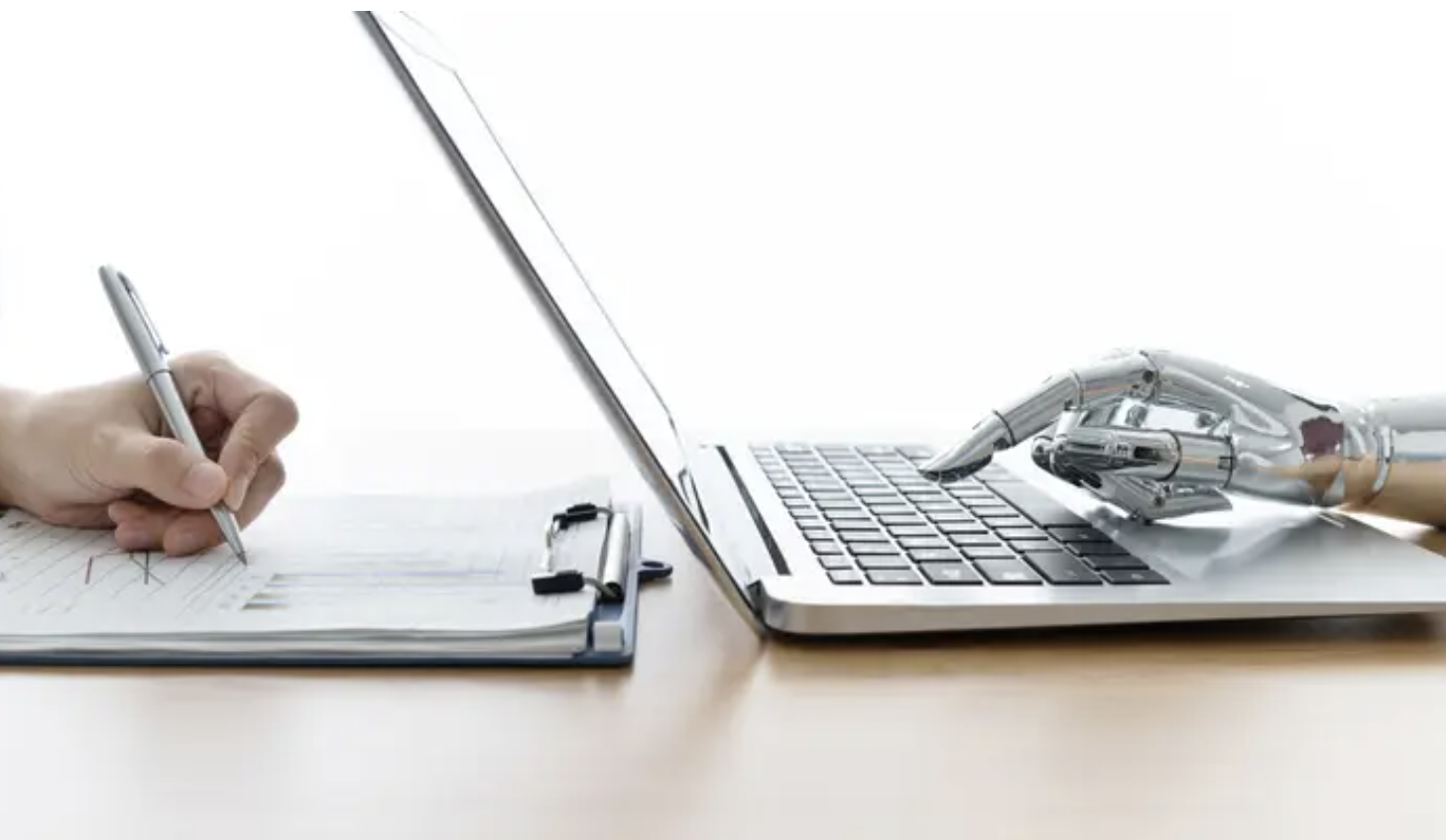 a human hand writing on a notepad next to a robot hand typing on a laptop