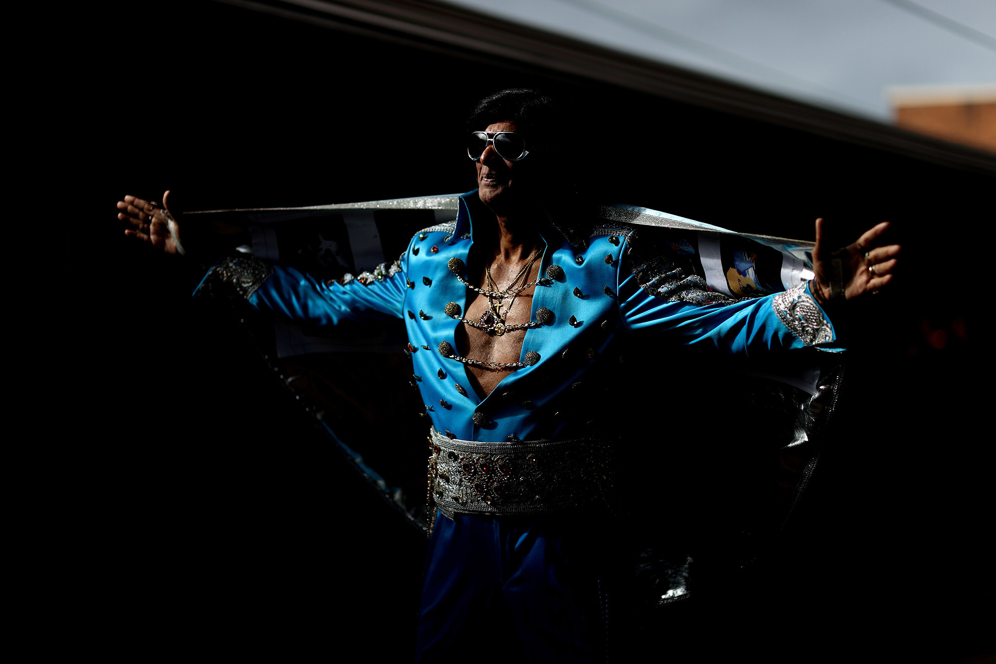 An Elvis impersonator in an open deep v stands in the shadows
