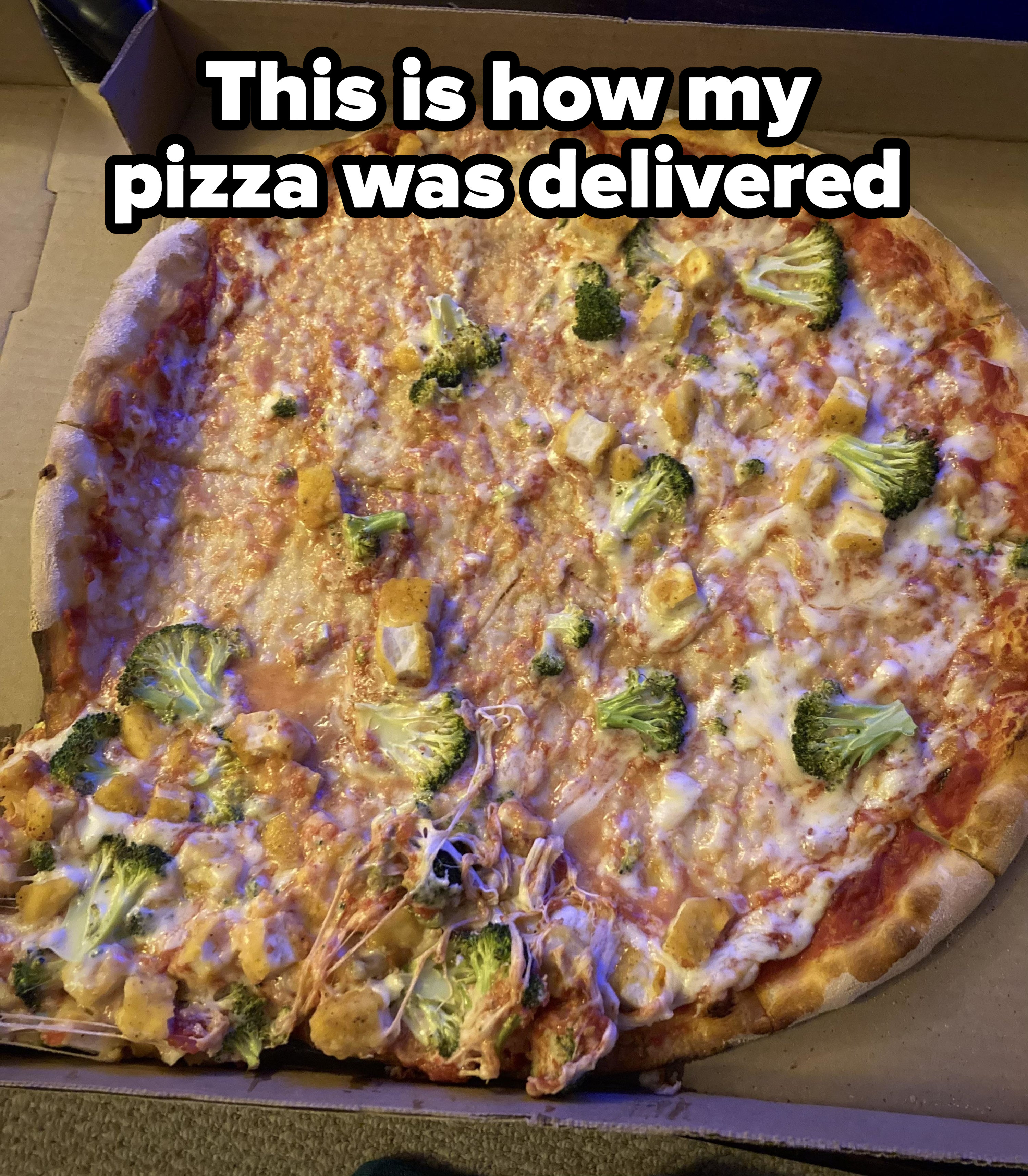 A pizza pie in the container with most of the toppings—cheese and broccoli—slid to the side
