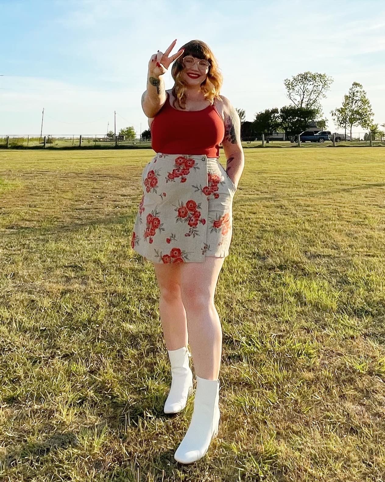 A reviewer wearing white boots with red and white floral skirt and red top