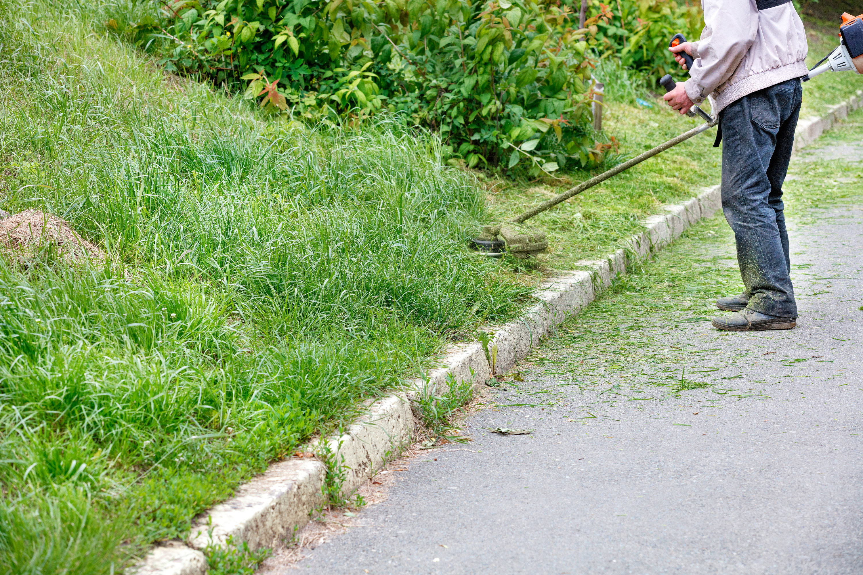 trimming grass along a steep hill near the curb of a driveway