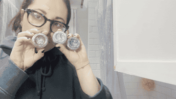 Me holding up small containers of glitter makeup