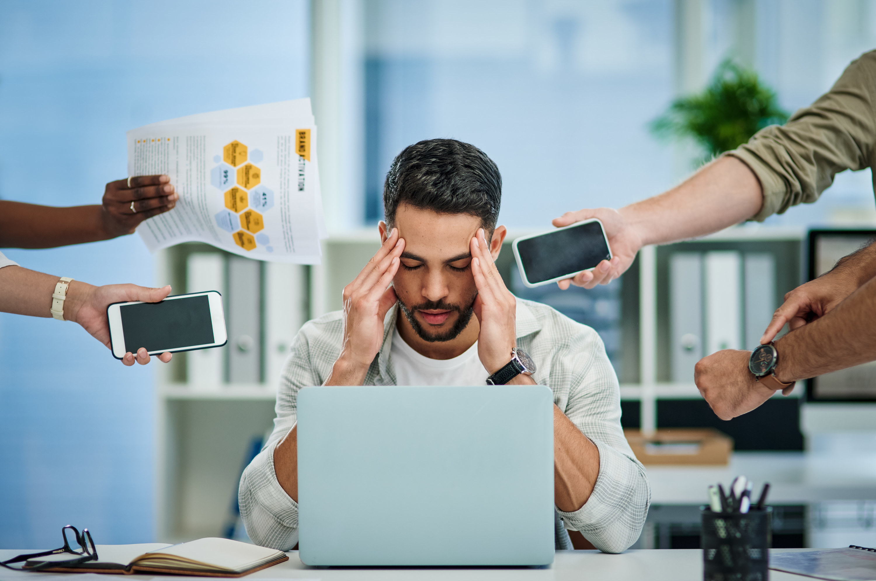 stressed out man sitting at a desk while coworkers hand him various tasks