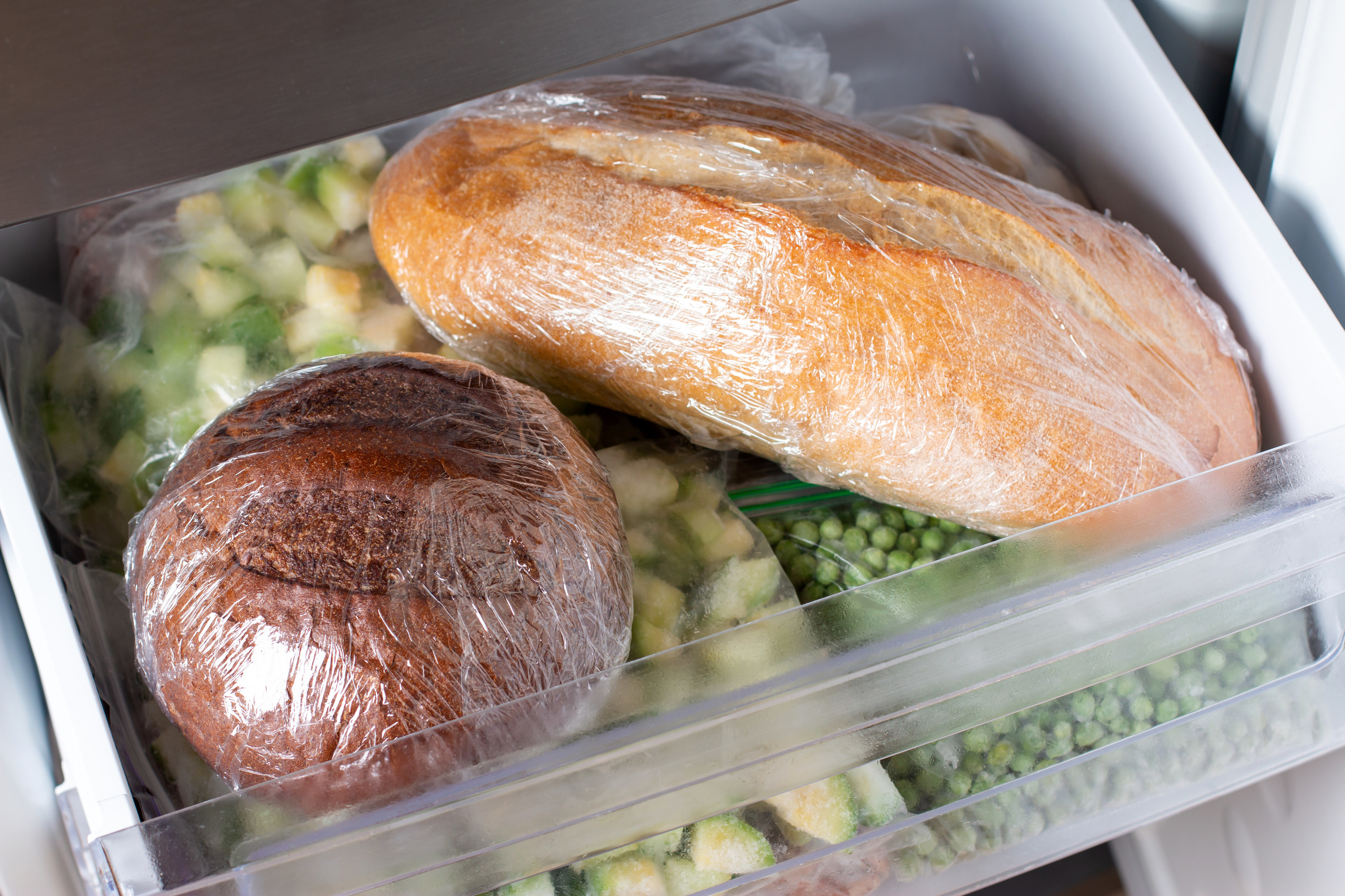 wrapping bread loaves tightly with plastic in a freezer